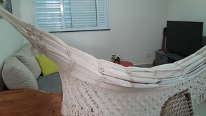 Una hamaca en una habitación con televisión, una guitarra y una ventana con persianas.