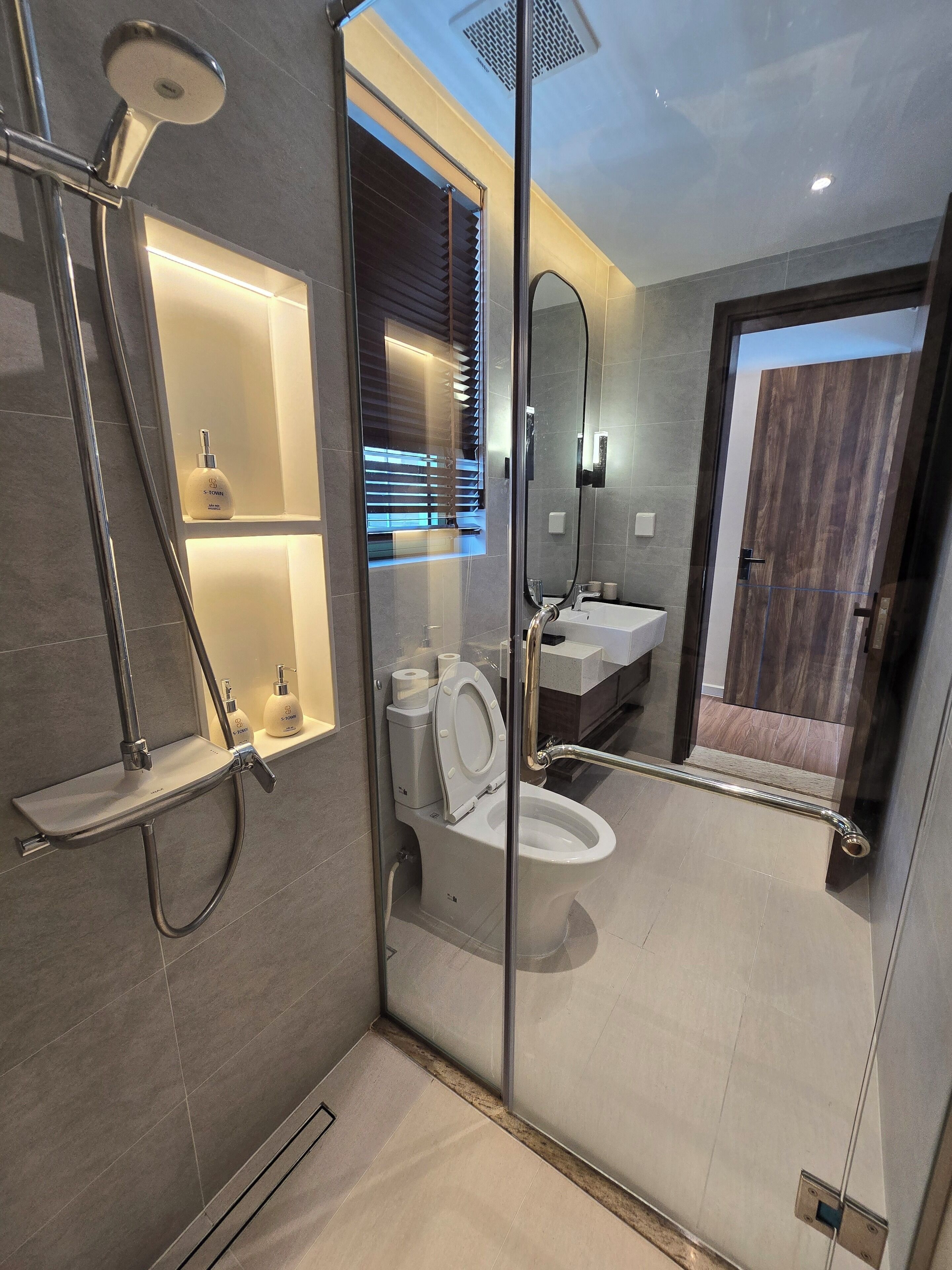 Un baño moderno con inodoro separado por mampara de vidrio, zona de ducha y tocador con espejo.