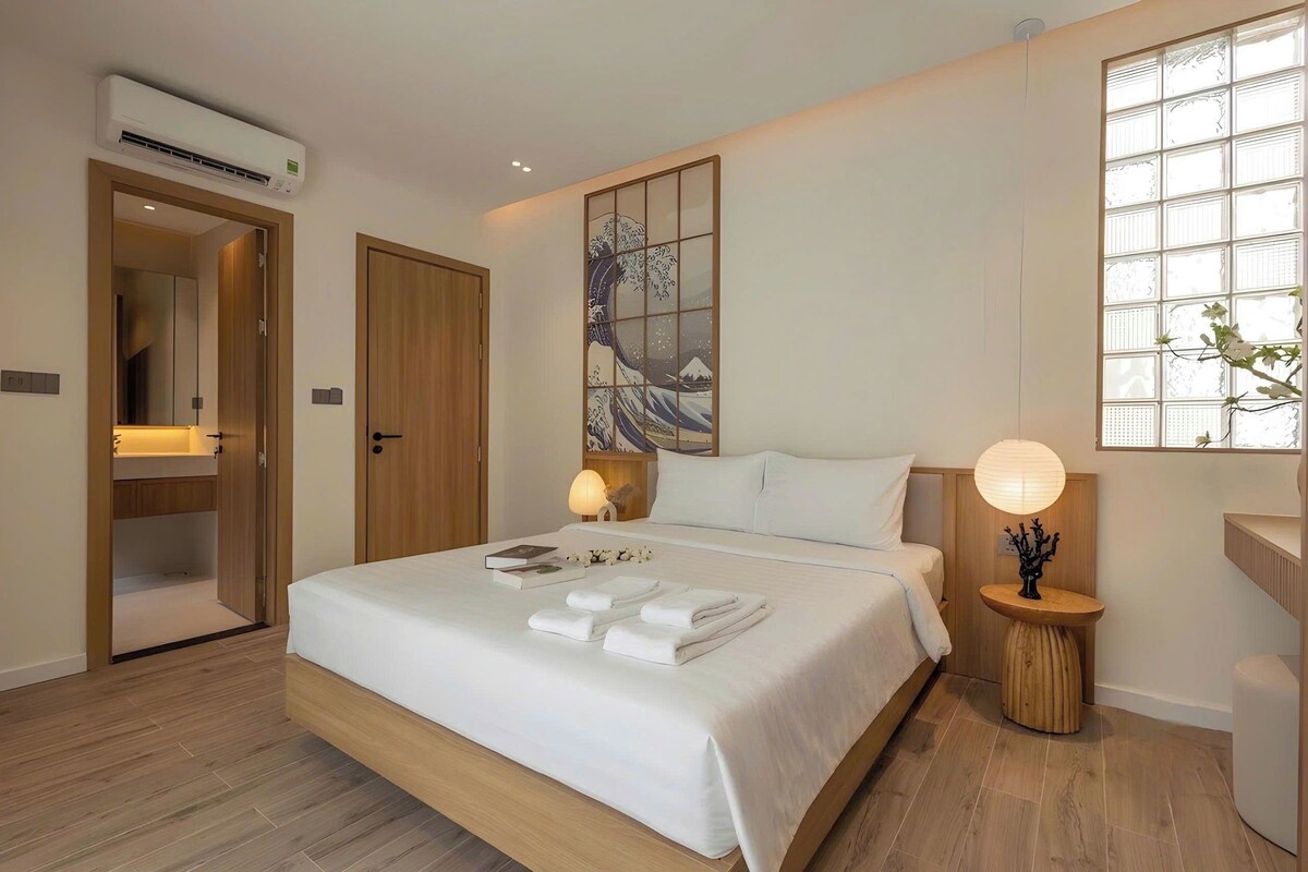 A hotel room with a bed, bedside lamps, a window with a view, and an air conditioning unit.