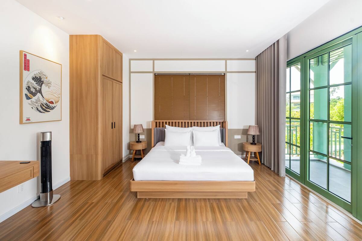 Una moderna camera d'hotel con pavimento in legno, un letto grande con lenzuola bianche, un armadio in legno, un termosifone e un'ampia finestra con vista sul verde.