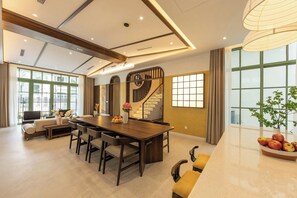 A spacious living room with a large wooden dining table, comfortable seating, a staircase, and large windows providing natural light. - Green Villas Tropical Phu Quoc (Phu Quoc)