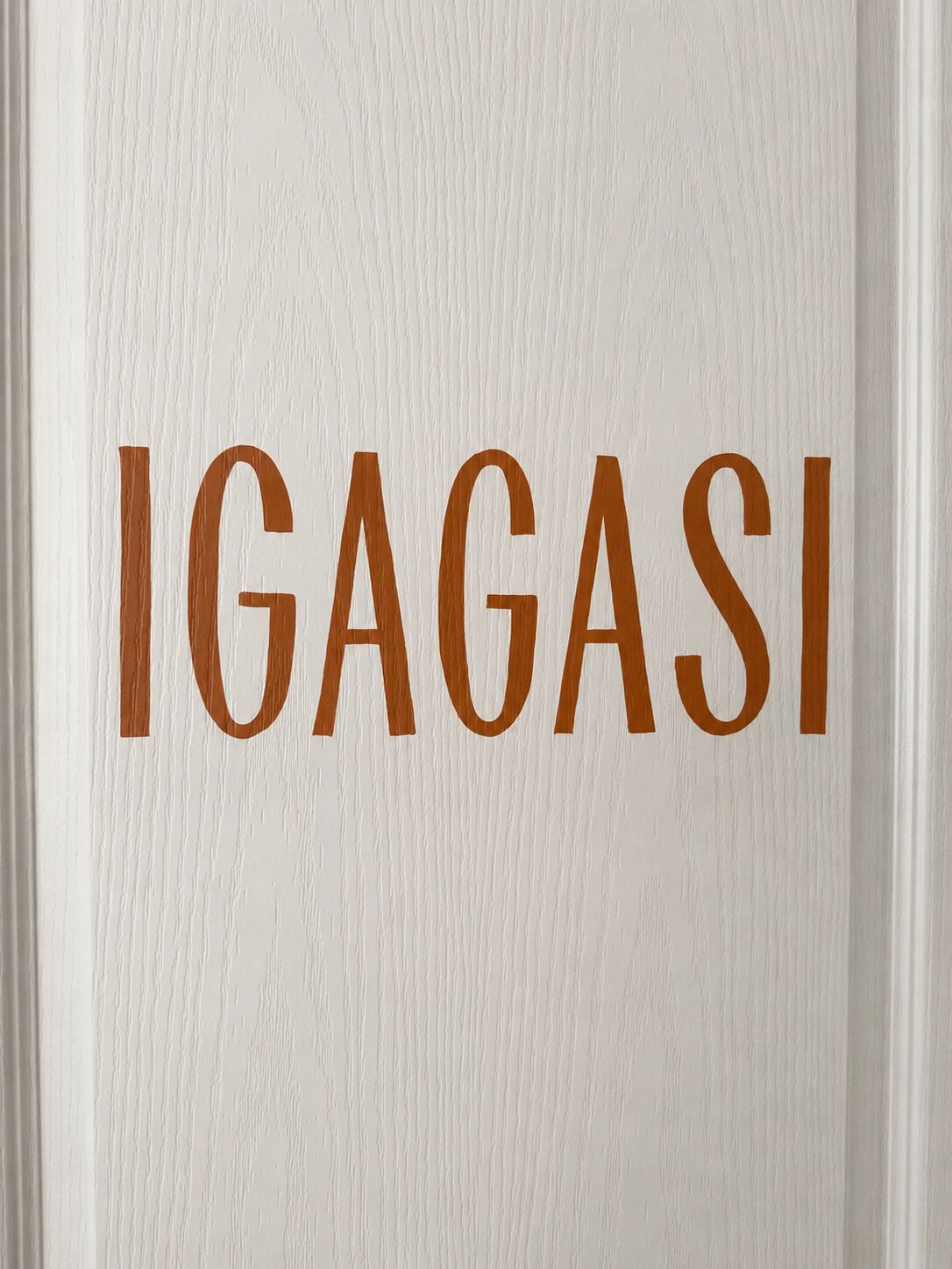 Une porte blanche sur laquelle est inscrit le mot « IGAGASI » en grandes lettres brunes.
