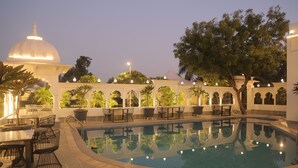 A pool area with a clear pool, surrounded by outdoor seating and potted plants. - Veer Garh Farms (Udaipur)