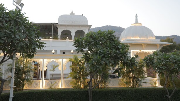 A white building with domed roofs and intricate architectural details, surrounded by well-maintained greenery. - Veer Garh Farms (Udaipur)