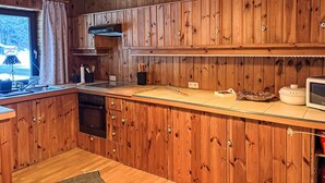 Cozinha de madeira com forno embutido, pia e janela com cortinas.