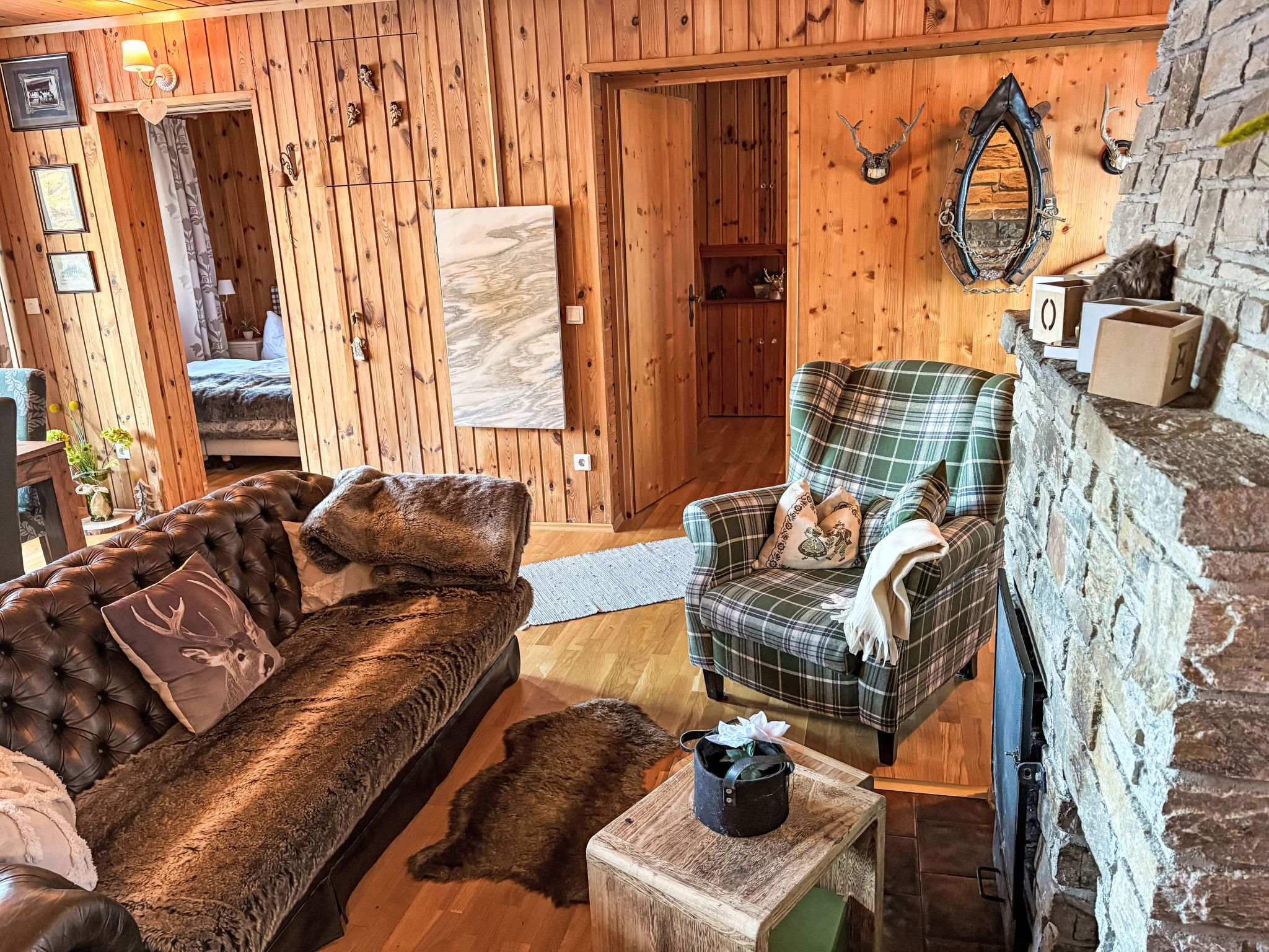 A cozy room with a brown leather sofa, plaid armchair, and a small wooden table with a black bag.
