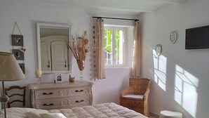 Une chambre à coucher avec un lit, une commode, une chaise et une fenêtre avec des rideaux.