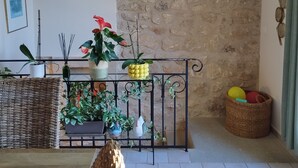 Une pièce avec un mur en pierre, un ventilateur de plafond, une chaise en osier et diverses plantes en pot.