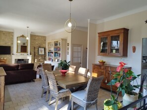 Amplia sala de estar con chimenea, comedor con sillas de mimbre, estantería y área de cocina con un armario.