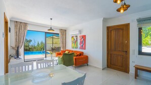 A modern living room with a pool view, a dining area, and a wooden door. - Swim, Sauna, Sea: An Exclusive Forest Sanctuary with Mediterranean Panoramas (antalya)
