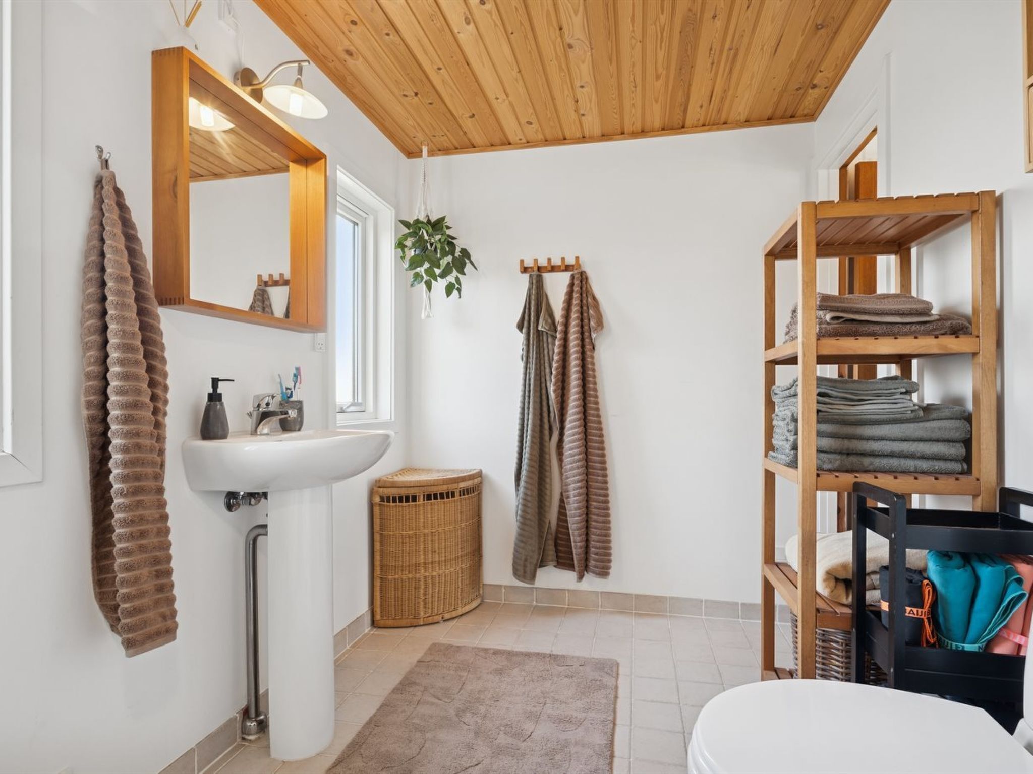 Ein Badezimmer mit Holzboden, weißen Wänden, einem Waschbecken, einem Spiegel, einer Ablage mit Handtüchern und einem Korbwäscheschrank.