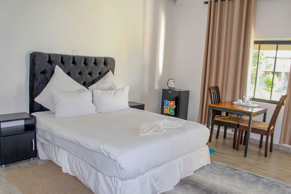 Een hotelkamer met een groot bed, een bureau met stoel, een klein kastje en een raam met gordijnen.