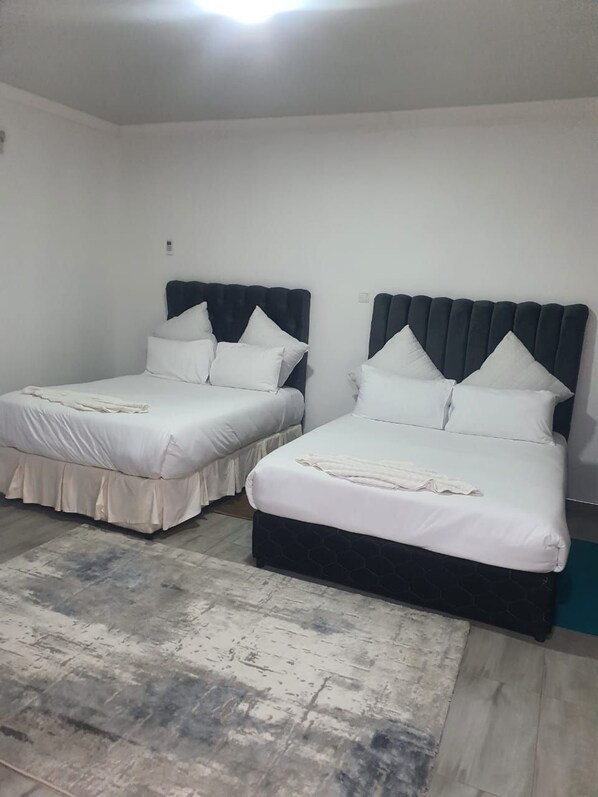 Une chambre avec deux lits, chacun doté d’une tête de lit sombre et de draps blancs.