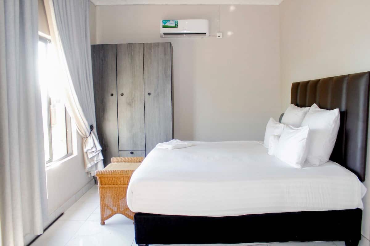 Een hotelkamer met een bed, een kledingkast, een rieten stoel en een airconditioner.