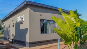 A single-story building with a flat roof, a window with curtains, and a small air conditioning unit mounted on the wall. - Tou Safari Lodge (Livingstone)