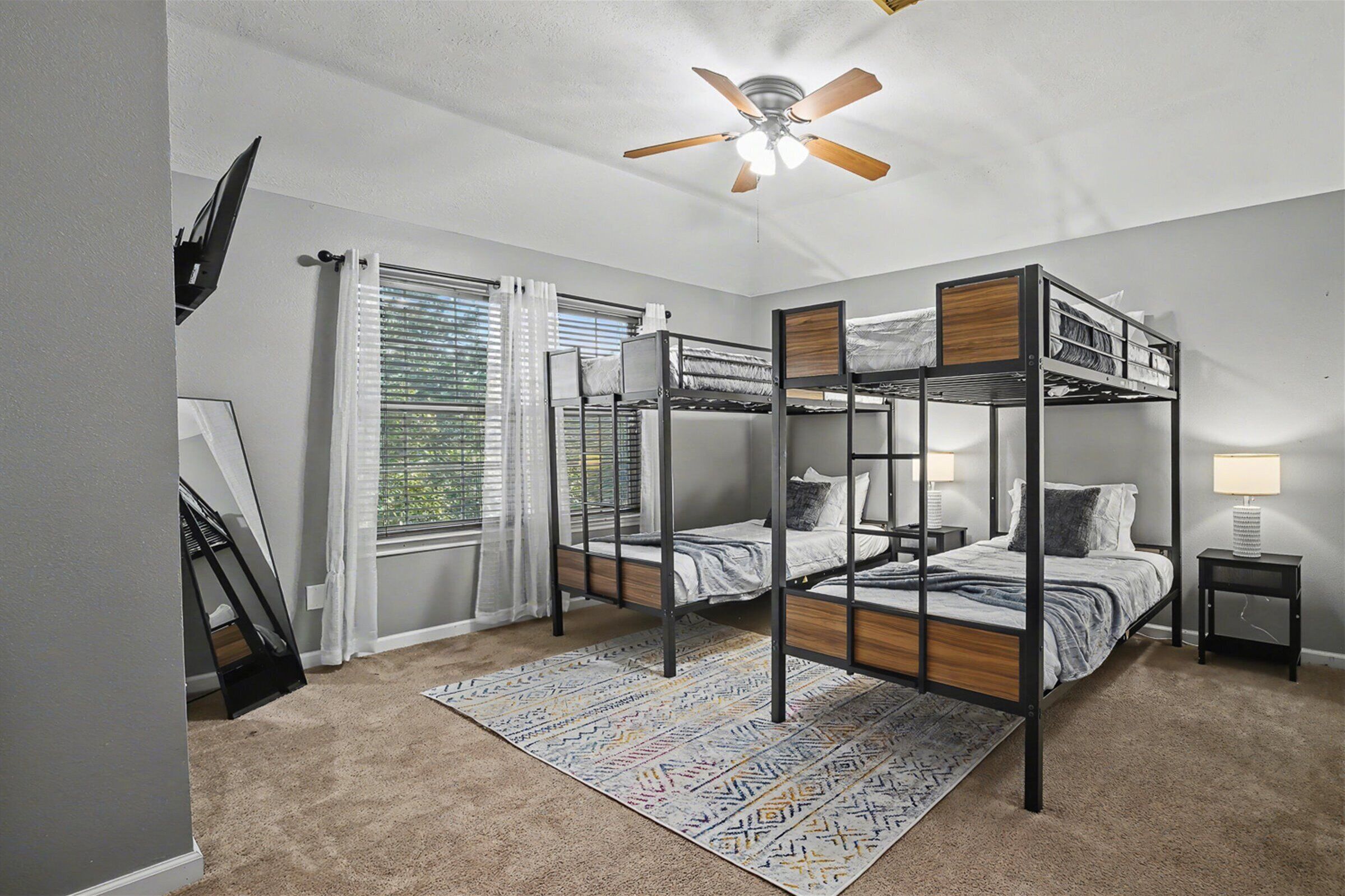 A bedroom with bunk beds, a ceiling fan, a window with blinds, and a patterned rug.