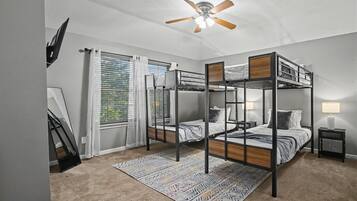 A bedroom with bunk beds, a ceiling fan, a window with blinds, and a patterned rug.
