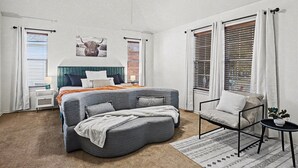 A bedroom with a curved bed, a chair, a small table, and a ceiling fan.