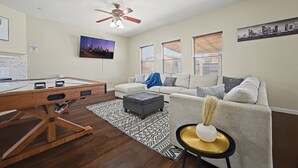 A living room with a pool table, a ceiling fan, a sofa, and a cityscape painting.