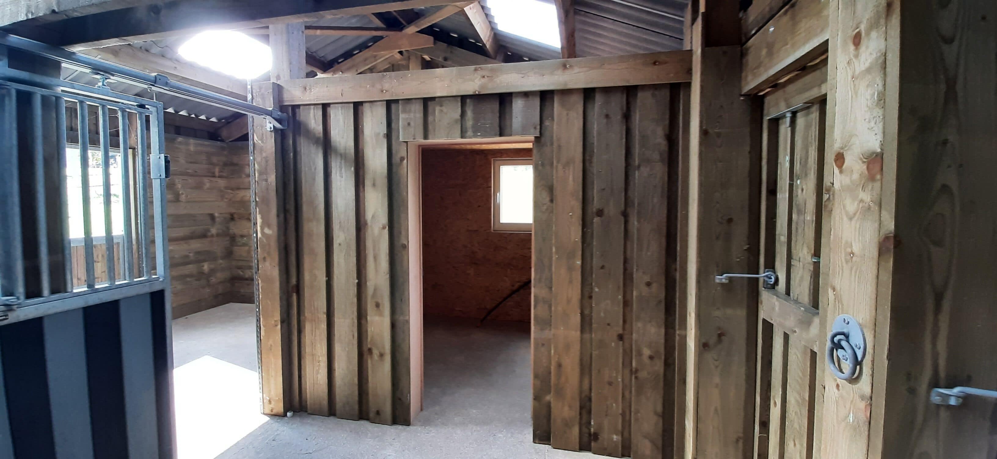 Interior de celeiro de madeira com portão de metal, porta com puxador de metal e janela.
