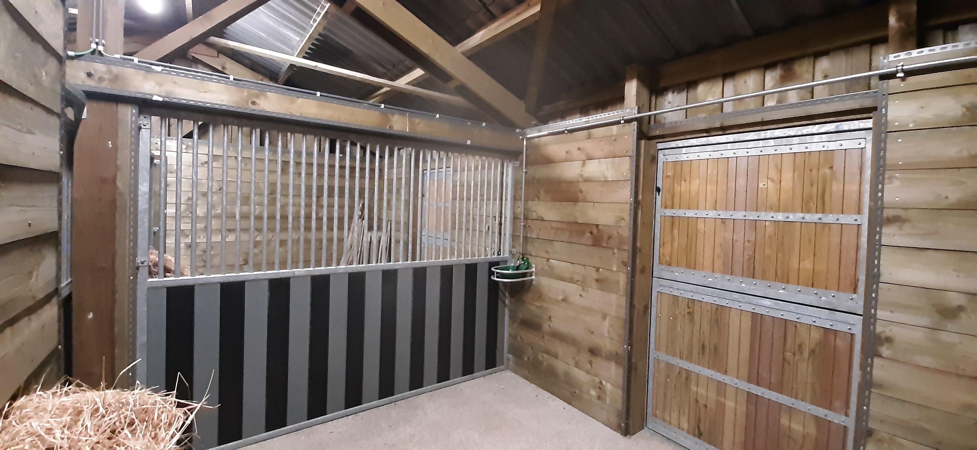 A barn interior with metal gates, wooden walls, and a hay bale.