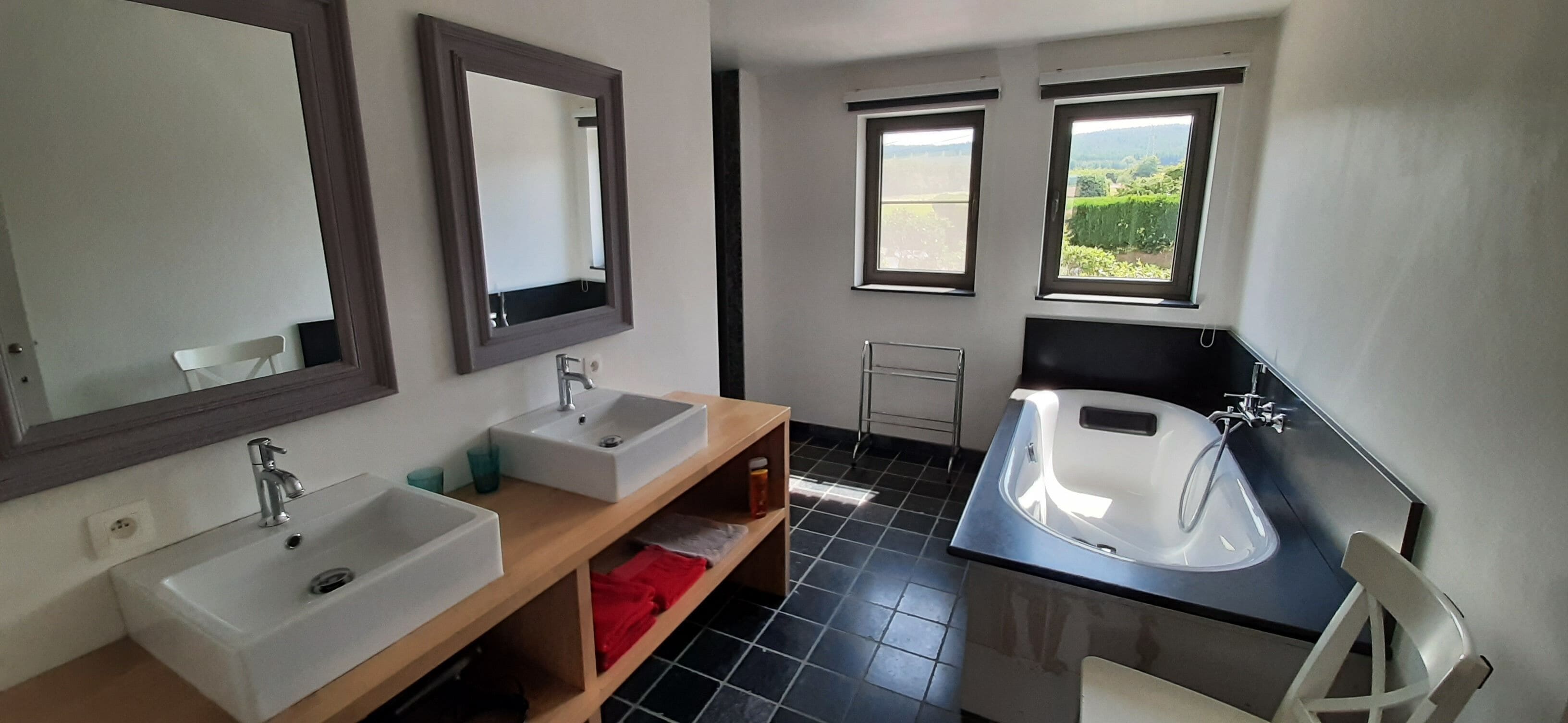 Une salle de bain avec deux lavabos, un grand miroir et deux fenêtres.