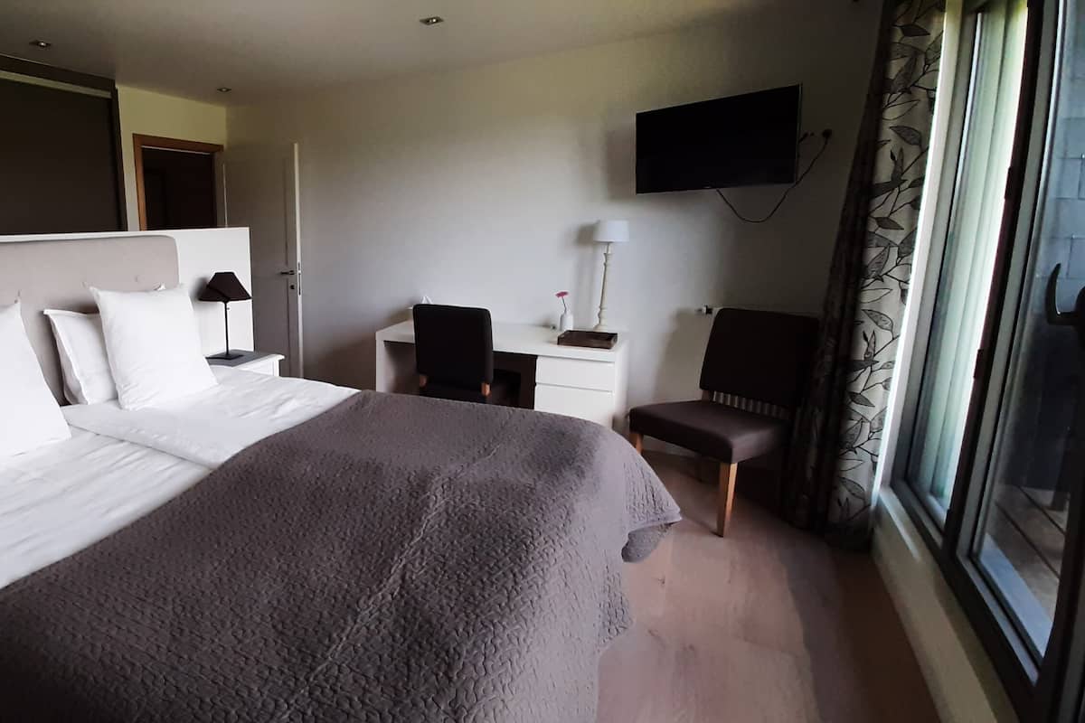 A hotel room with a bed, bedside table, chair, desk, TV, and window.