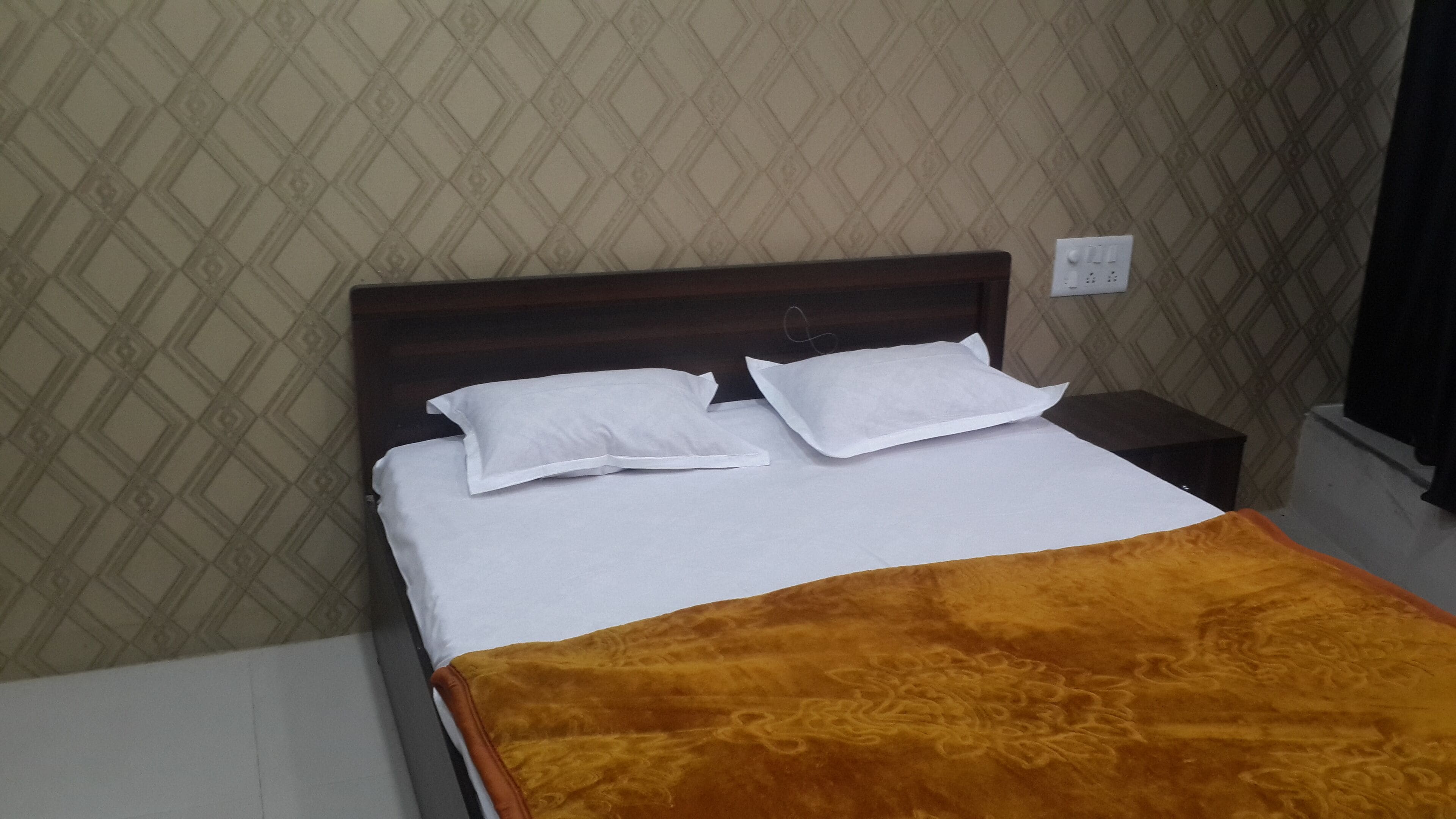 A neatly made bed with white linens and a brown throw blanket, a wooden headboard, and a small bedside table with a lamp.