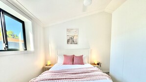 Un lit bien fait, avec un oreiller à carreaux blancs et roses, deux lampes de chevet et un tableau encadré accroché au mur.