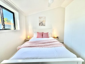 Un letto rifatto con un cuscino bianco e rosa a quadretti, due lampade da comodino e un quadro appeso al muro.