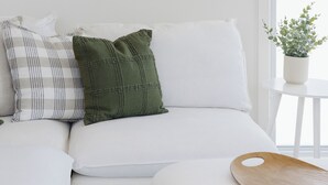 Een witte bank met gestreepte en effen kussens, een houten dienblad en een lijstwerk erboven.