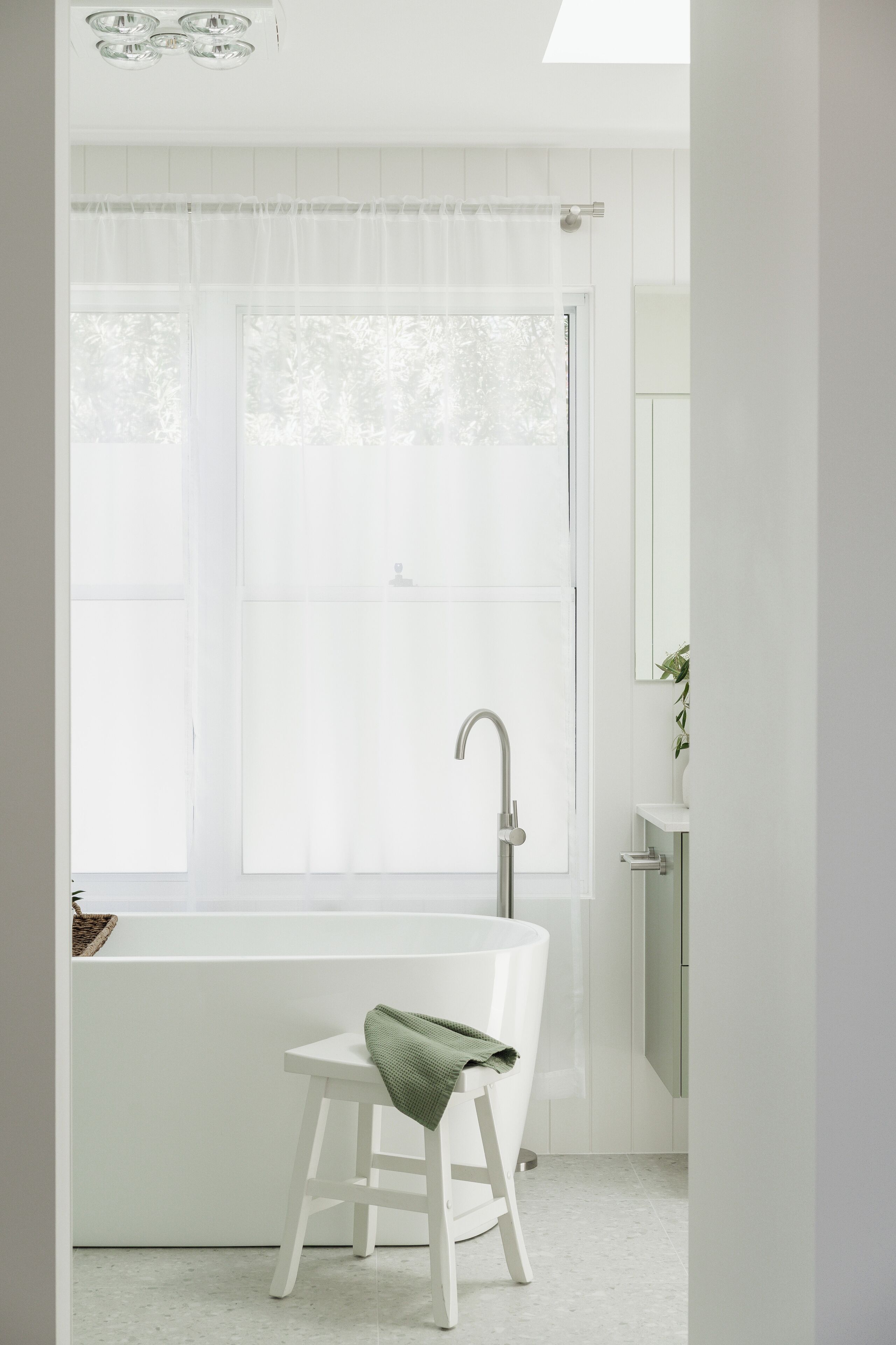 A bathroom with a white bathtub, a white sink, and a window with sheer curtains.