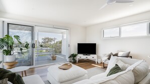 Een moderne woonkamer met een flatscreen televisie, witte banken, een salontafel en een balkon met potplanten.