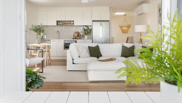 Een moderne woonkamer met een witte bank, een eettafel met stoelen, en een keuken met witte kasten en een koelkast.