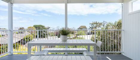 A covered outdoor area with a white table and bench, a potted plant, and a view of surrounding houses.