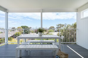 Un espace extérieur abrité, avec une table et un banc blancs, une plante en pot et une vue sur les maisons environnantes.