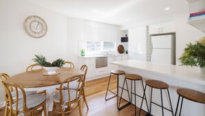 Een moderne keuken met witte kasten, een houten eettafel met vier stoelen, en een bar met krukjes.