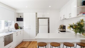 Een moderne keuken met witte kasten, een centraal eiland met krukken, een ingebouwde magnetron en een koelkast.