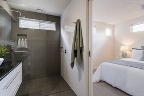 Une salle de bain moderne avec une douche, un lavabo et un miroir. Une serviette est accrochée au mur et une petite étagère contient des articles de toilette.