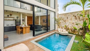 Ett modernt hus med en swimmingpool, ett matområde och ett kök som syns genom stora glasdörrar.