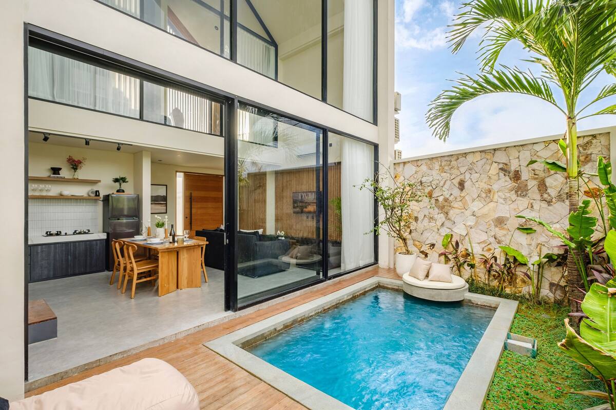 A modern house with a swimming pool, a dining area, and a kitchen visible through large glass doors.