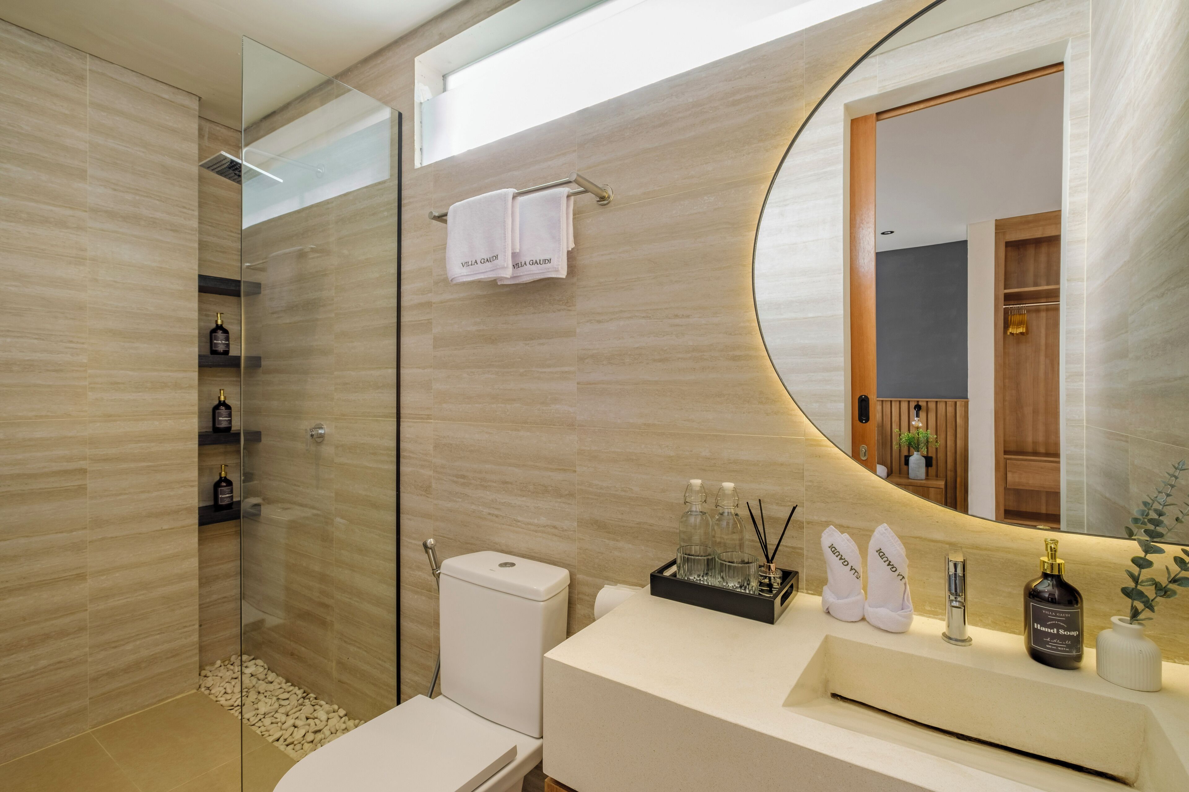 Un baño moderno con cabina de ducha de vidrio, un inodoro blanco, un lavabo con espejo y un estante con artículos de aseo.