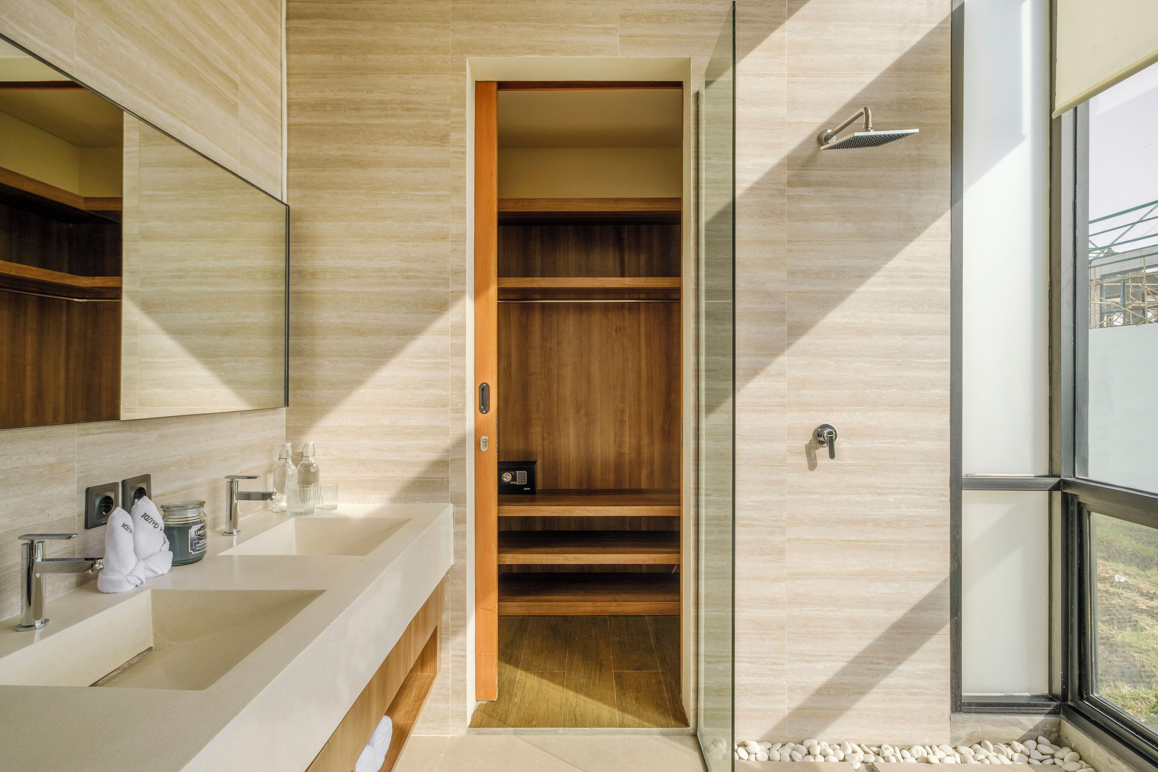 A modern bathroom with a large mirror, a walk-in shower, and a built-in wooden shelf.