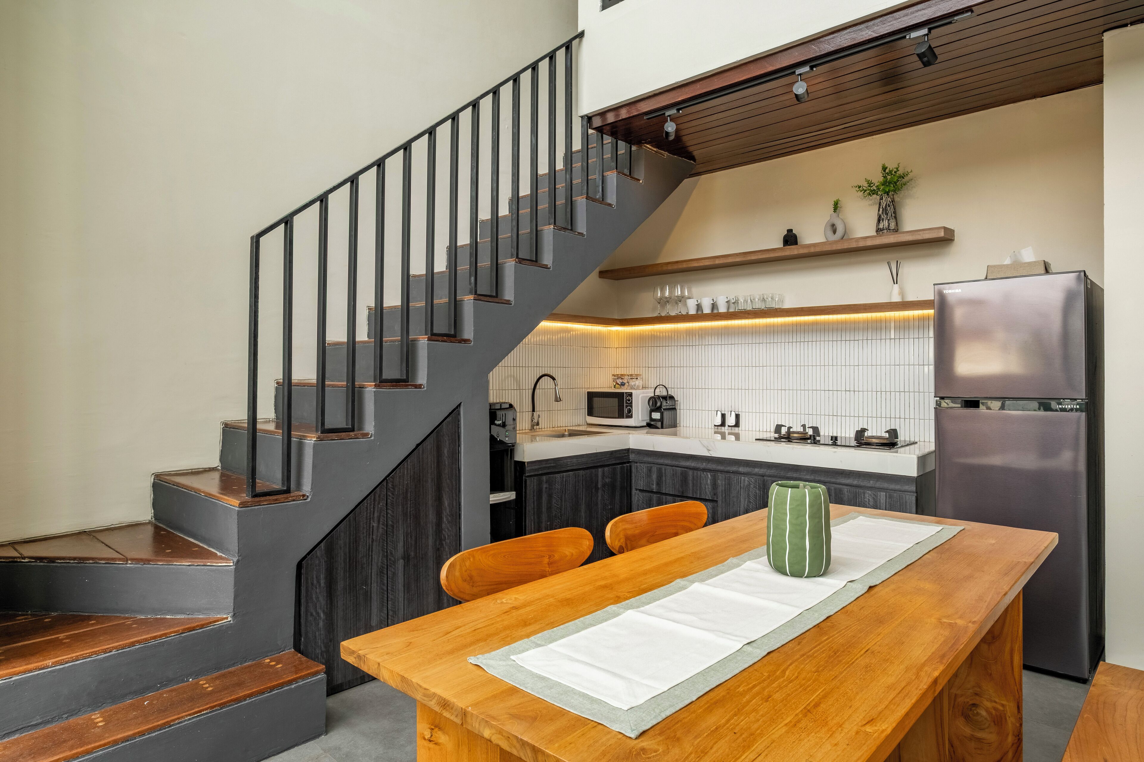 A modern kitchen with a wooden dining table, a built-in oven, and a stainless steel refrigerator.