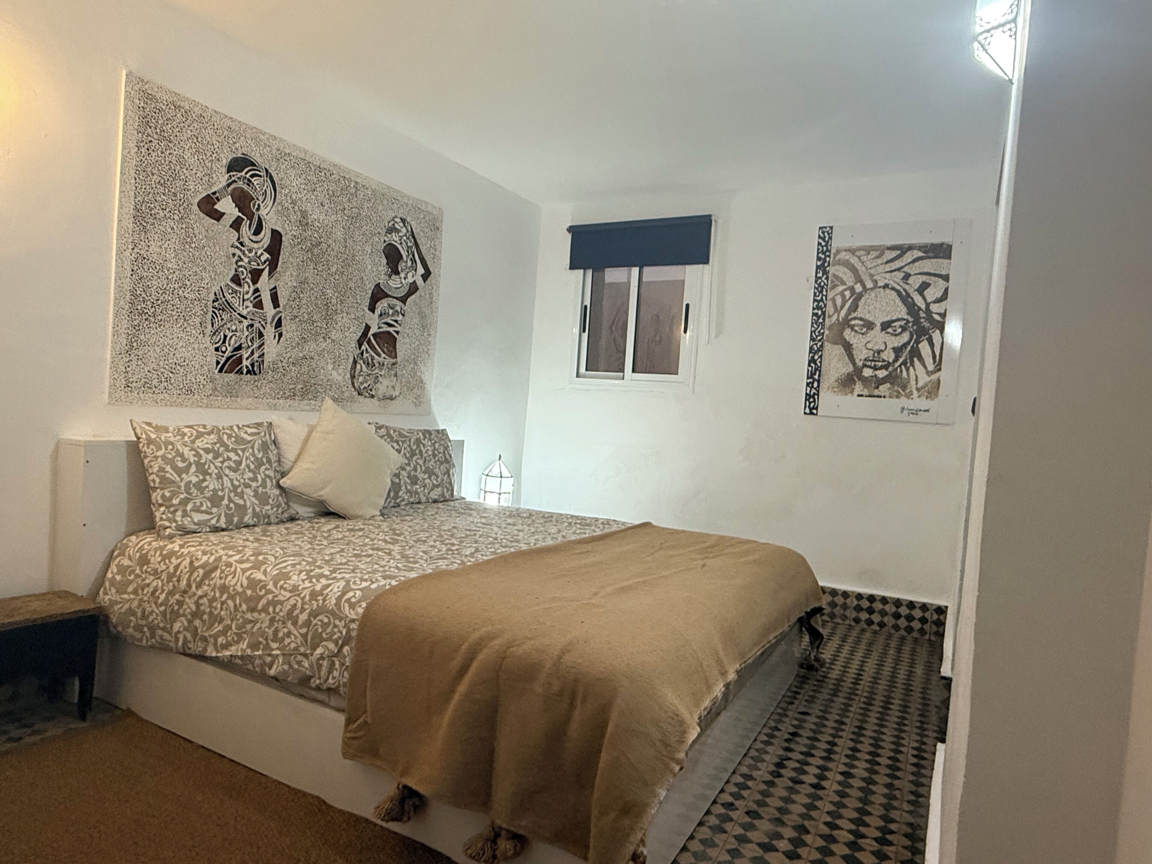 Un dormitorio con cama, ropa de cama estampada, una ventana y obras de arte en las paredes.