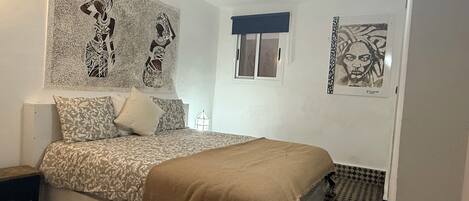 A bedroom with a bed, patterned bedding, a window, and artwork on the walls.