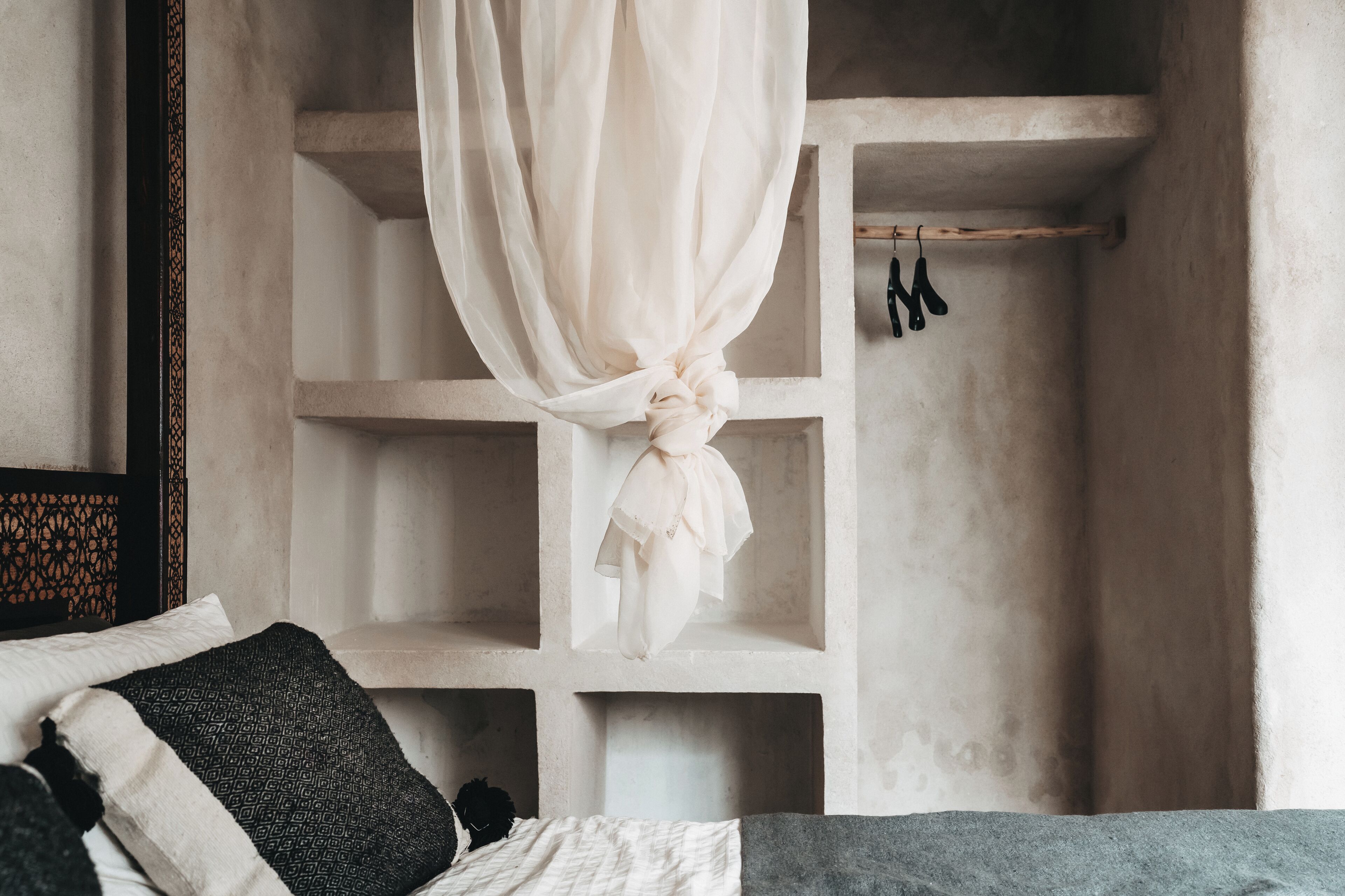 Une chambre à coucher avec un lit, des oreillers, un dais suspendu et une étagère sur laquelle sont accrochés divers objets.