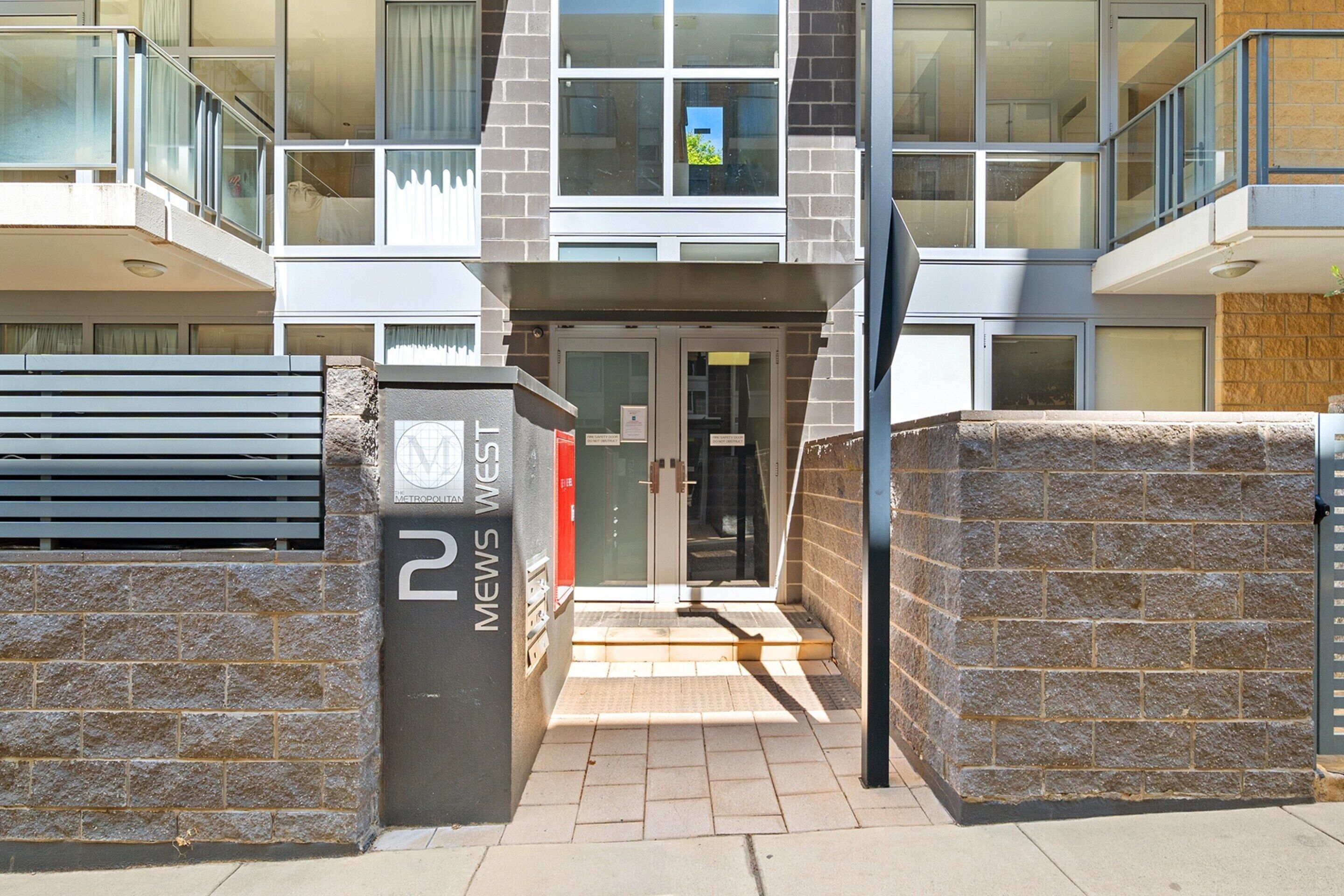 A modern building entrance with a glass door, a stone wall, and a metal gate.