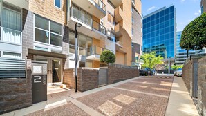 Un moderno edificio residenziale con facciata in mattoni, ingresso carrabile e un piccolo albero di fronte.