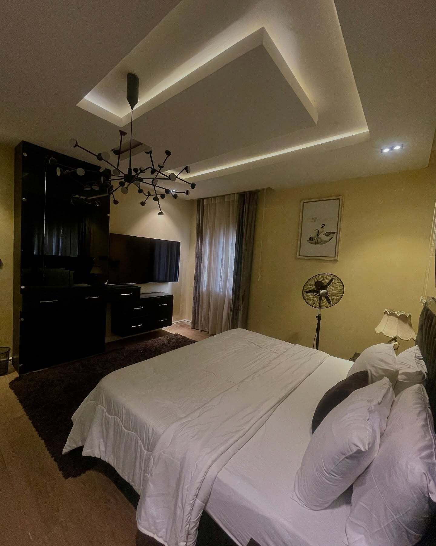 Ein modernes Schlafzimmer mit Bett, Fernseher, Deckenventilator und einem großen Spiegel.